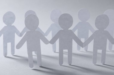 Takım çalışması konsepti. Açık gri arka planda el ele tutuşan insanların kağıt figürleri, yakın plan