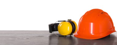 Beyaz arka plana karşı ahşap masanın üzerinde sert şapka ve kulaklık. Güvenlik ekipmanları