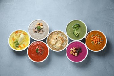 Lezzetli çorba ve farklı krema çorbaları gri masada, düz yerde.