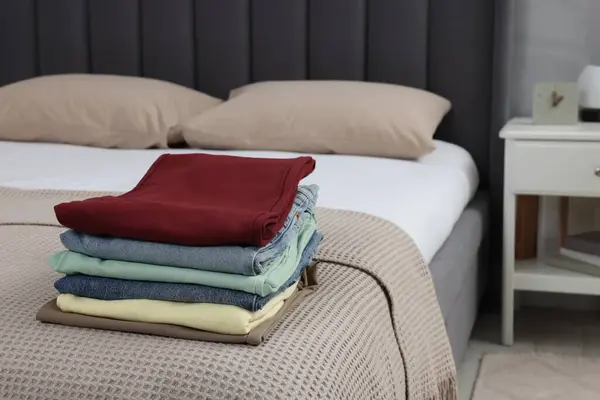 Stack of folded clothes on bed indoors, space for text