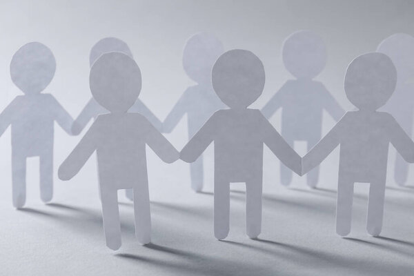 Концепция командной работы. Бумажные фигуры людей, держащихся за руки на светло-сером фоне, крупным планом