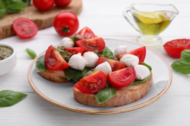 Mozzarella, domates, fesleğen ve pesto soslu lezzetli Caprese sandviçleri beyaz ahşap masada.