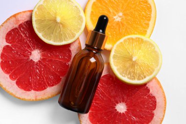 Beyaz arka planda bir şişe kozmetik serumu ve dilimlenmiş narenciye meyvesi.
