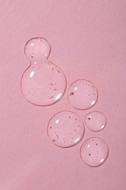 Pembe arka planda kozmetik serumu damlaları, üst görünüm.