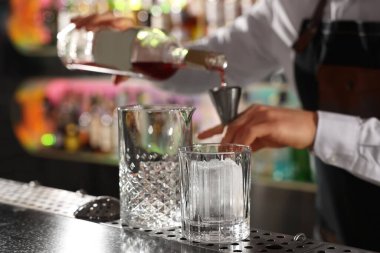 Kokteyl yapımı. Barmen bardaki tezgahta barmenden alkole geçiyor, seçici odaklanma.