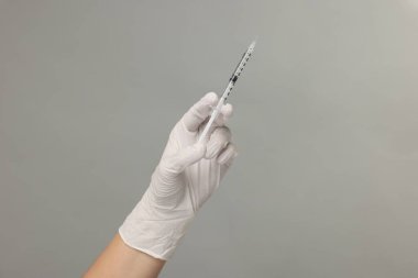 Gri arka planda tıbbi şırınga tutan doktor, yakın plan.
