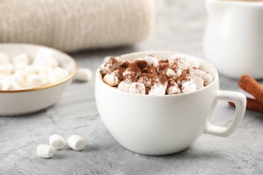 Bir fincan aromatik sıcak çikolata, marshmallowlu ve kakao tozlu gri masa, yakın plan.