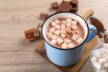 Marşmelovlu bir fincan aromatik sıcak çikolata ve ahşap masada kakao tozu, yakın plan. Metin için boşluk