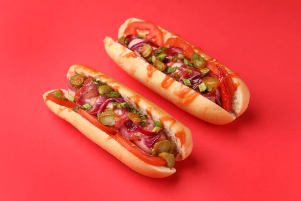 Tasty hot dogs with onion, tomato, pickles and sauce on red background