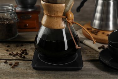 Glass chemex coffeemaker with coffee and beans on wooden table, closeup clipart