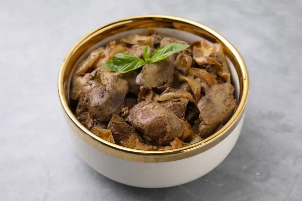 Delicious fried chicken liver with onion in bowl on light grey table, closeup