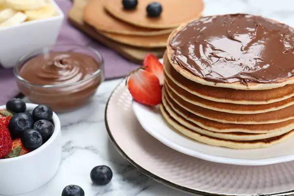 Tasty pancakes with chocolate paste and berries on white marble table, closeup