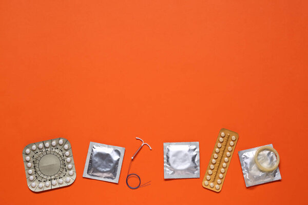Противозачаточные таблетки, презервативы и внутриутробное устройство на оранжевом фоне, квартира с местом для текста. Различные методы контрацепции