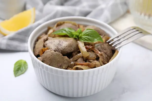 Delicious fried chicken liver with onion and basil in bowl on white table, closeup