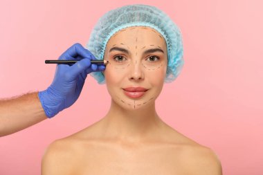 Pembe arka planda estetik ameliyat için kalem hazırlayan bir doktor.