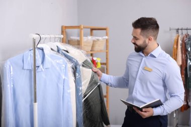 Kuru temizleme servisi. Defterli mutlu işçi, kapalı alandan palto alıyor.