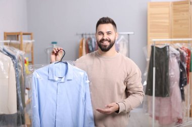 Kuru temizleme servisi. Kapalı mekanda plastik torba içinde gömlek tutan mutlu adam.