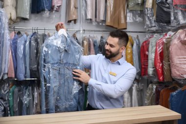 Kuru temizleme servisi. Kapalı mekanda plastik torbada kot ceketli askı tutan mutlu işçi.
