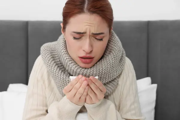 Woman with tissue coughing on bed. Cold symptoms