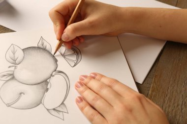 Tahta masadaki kağıda meyve çizen grafit kalemli kadın, yakın plan.