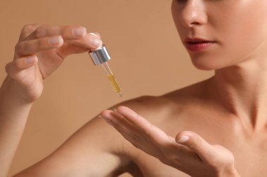 Bej arka planda eline kozmetik serumu süren bir kadın.