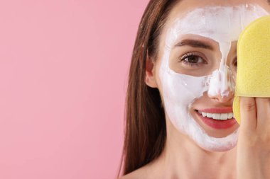 Yüz maskesi ve pembe arka planda süngeri olan mutlu genç kadın, mesaj için yakın çekim alanı