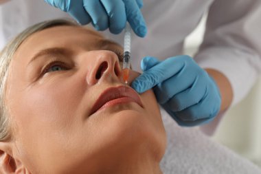 Doktor klinikteki yaşlı kadına dudak iğnesi yapıyor, yakın plan. Estetik ameliyat