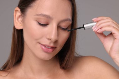 Gri arka planda kirpiklere serum süren güzel bir kadın. Yakın plan.
