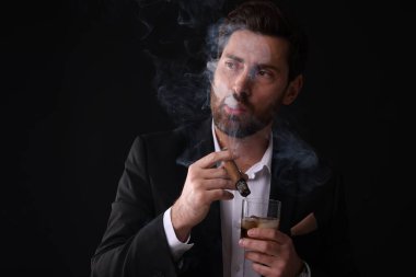 Siyah arka planda puro içen zarif takım elbiseli yakışıklı bir adam.