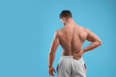 Man suffering from back pain on light blue background, back view. Space for text clipart
