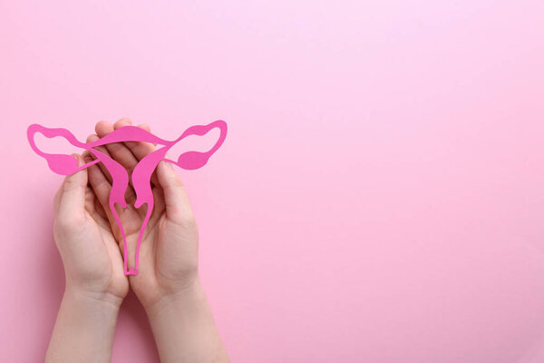 Reproductive medicine. Woman holding paper uterus on pink background, top view with space for text