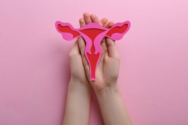 Reproductive medicine. Woman holding paper uterus on pink background, top view