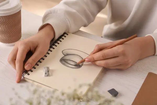 テーブルのスケッチブックでグラファイト鉛筆でドリンクのカップを描く女性 クローズアップ — ストック写真