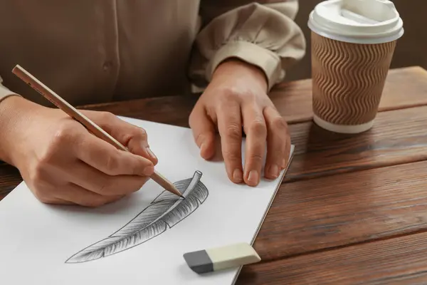 木のテーブルでスケッチブックのグラファイト鉛筆で羽を描く女性 クローズアップ — ストック写真