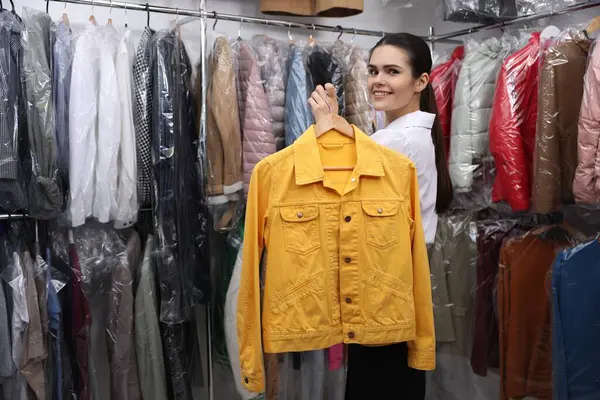 Dry-cleaning service. Happy worker holding hanger with jacket indoors