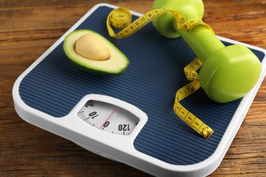 Sağlıklı beslenme. Ölçek, avokado, mezura ve ahşap masa üzerindeki dambıl, yakın çekim