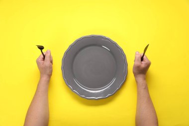 Çatallı, bıçaklı ve boş tabaklı adam sarı masada, üst tarafta.