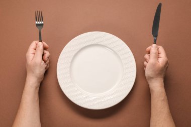 Kahverengi masada çatal bıçaklı ve boş tabaklı bir adam var.