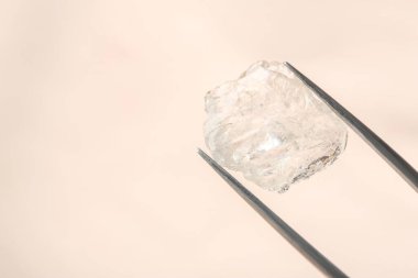 Bej arkaplanda parlak elmas olan cımbızlar, yakın plan.