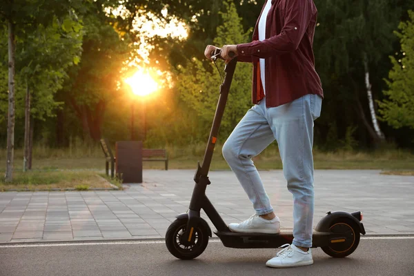 Man with modern electric kick scooter in park, closeup. Space for text