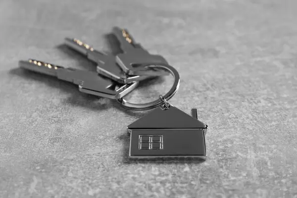Keys with keychain in shape of house on light grey table, closeup