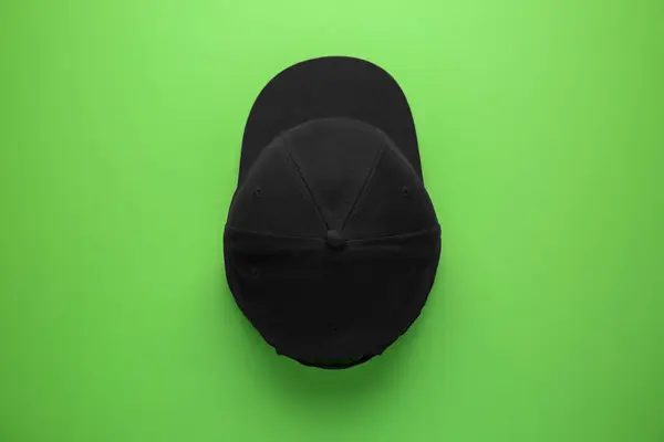 Stylish black baseball cap on light green background, top view