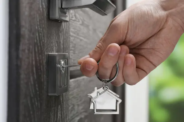 Man unlocking door with key outdoors, closeup
