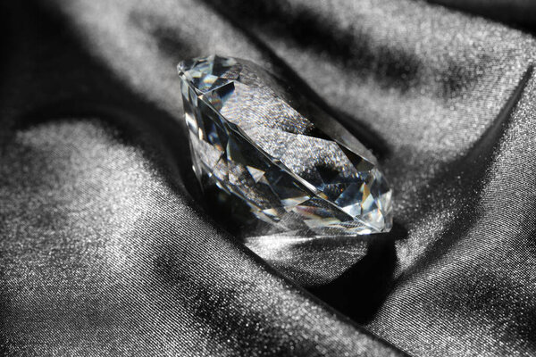 Beautiful shiny diamond on black silky fabric, closeup