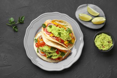 Siyah masada servis edilen guacamole ve sebzeli lezzetli tacolar.