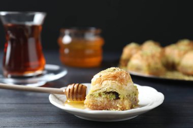 Lezzetli taze baklava ve siyah ahşap masada doğranmış fındıklı bal, yakın plan. Doğu tatlıları