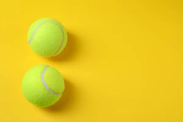 Two tennis balls on yellow background, above view. Space for text