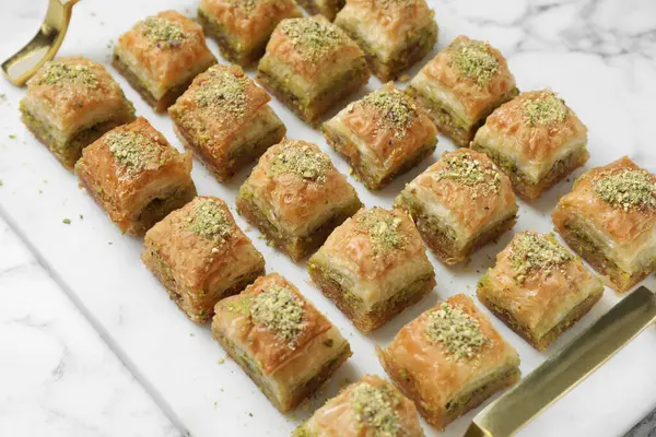 Delicious fresh baklava with chopped nuts on white marble table, closeup. Eastern sweets
