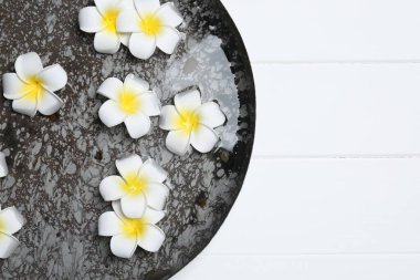 Beyaz ahşap masa üzerinde tesisat çiçekleri olan bir kase su, üst manzara ve yazı için yer. Spa tedavisi