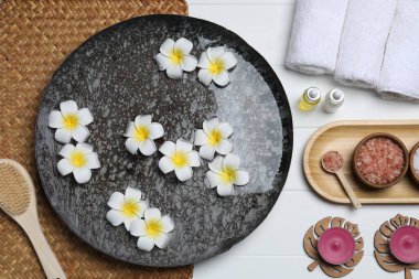 Çiçekli bir kase su ve beyaz ahşap masada farklı spa malzemeleri.